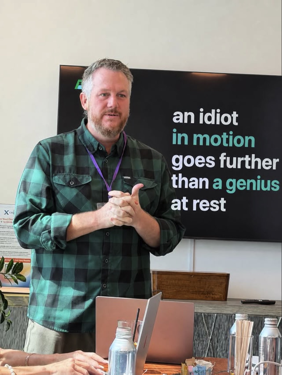 Rossco Paddison speaking to a room of founders beside a slide reading 'an idiot in motion goes further than a genius at rest'